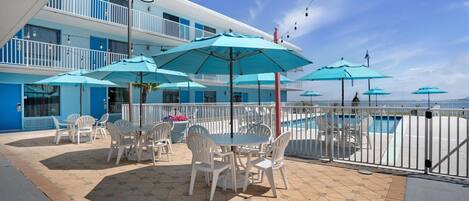 A rooftop patio with outdoor seating and umbrellas, overlooking a pool.