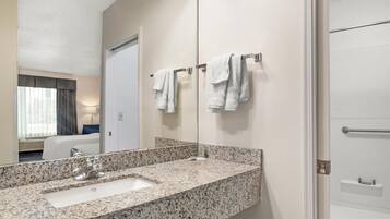 A hotel bathroom with a granite countertop sink, a large mirror, and two towels hanging on a towel rack.