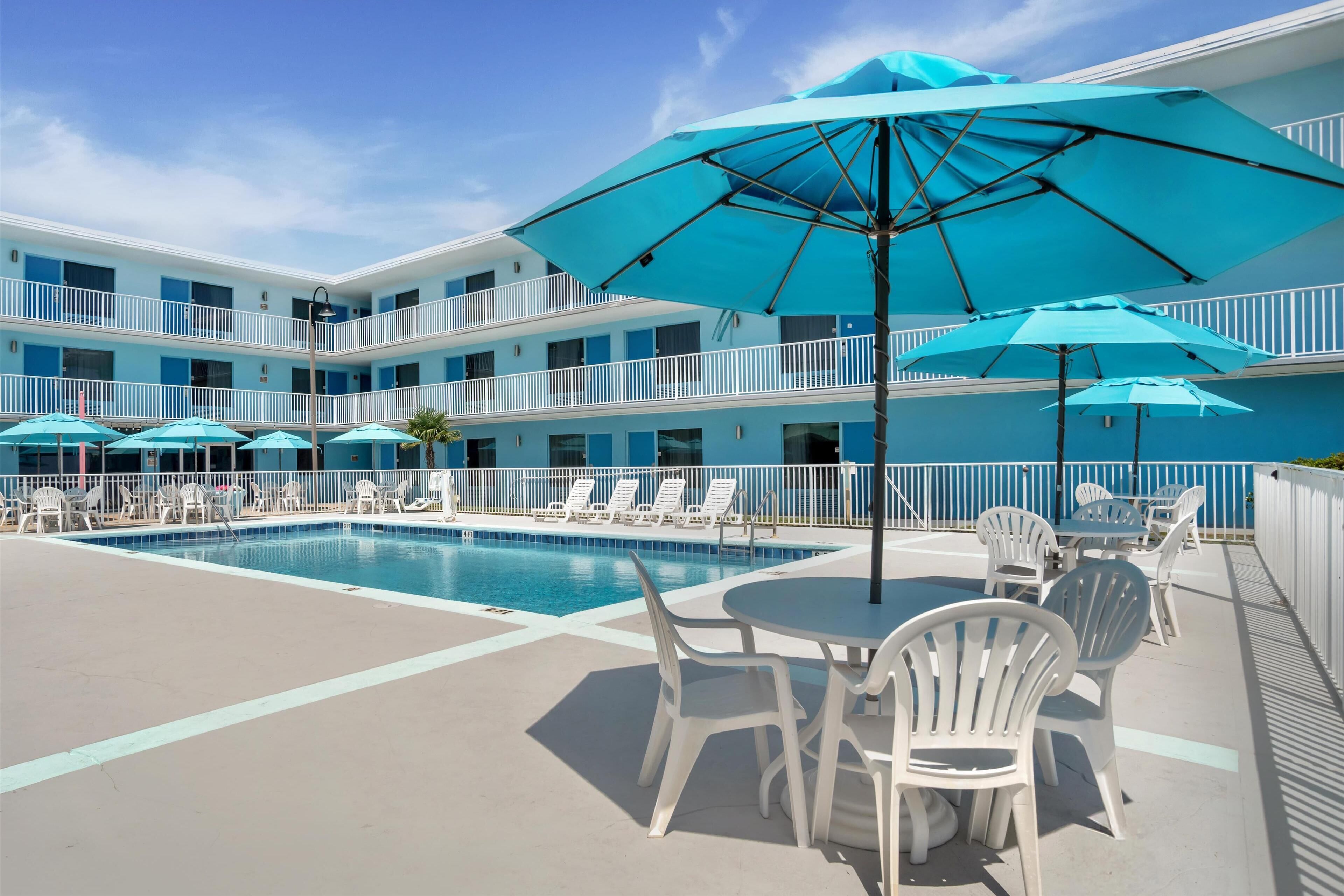 Un hotel con zona de piscina, mobiliario exterior y varios balcones.