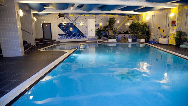 Una piscina interior con agua cristalina, paredes de azulejos y una escalera que conduce a una puerta.
