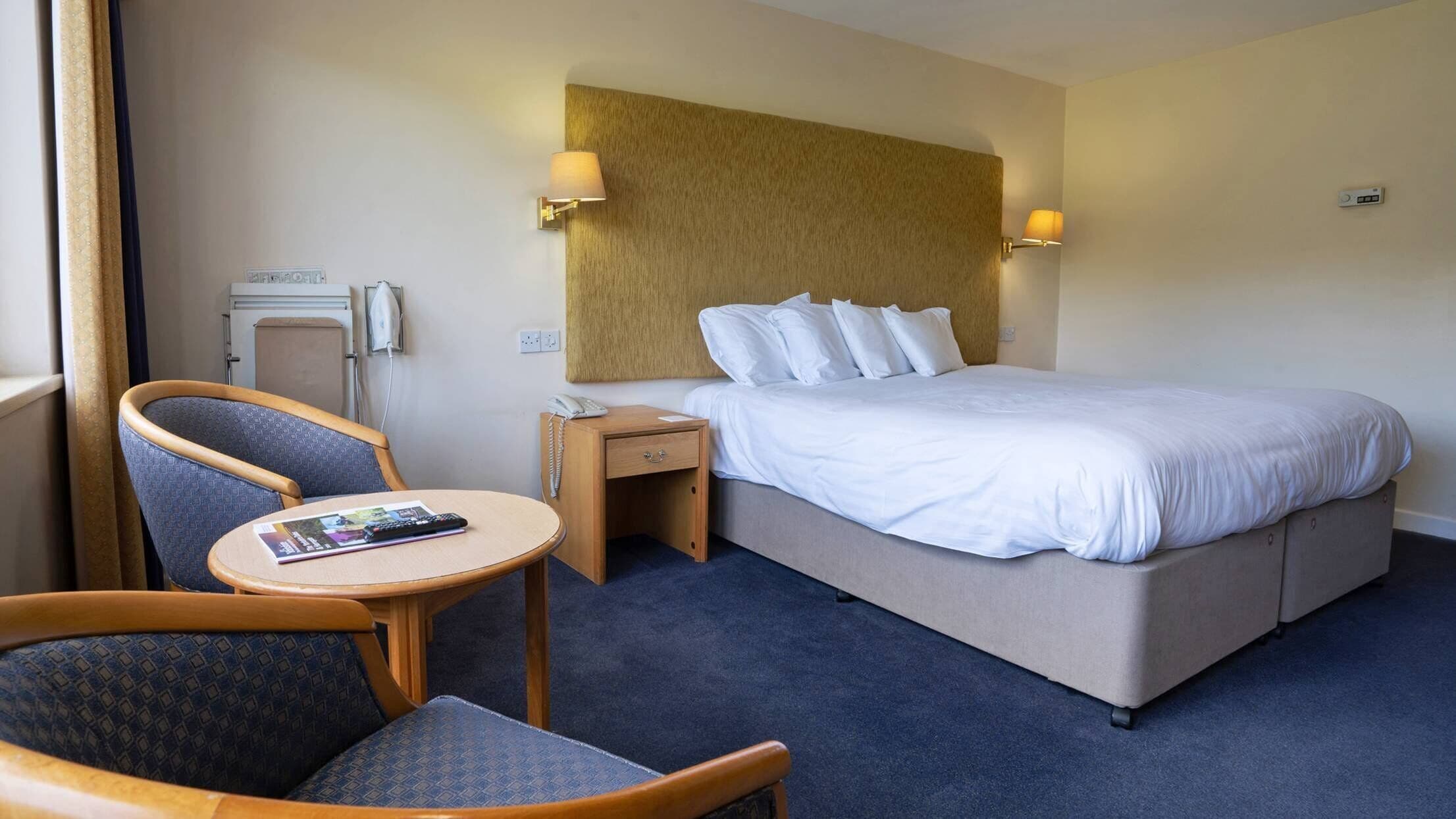 Una habitación de hotel con una cama, una silla, una mesita, una mesita de noche y una lámpara.