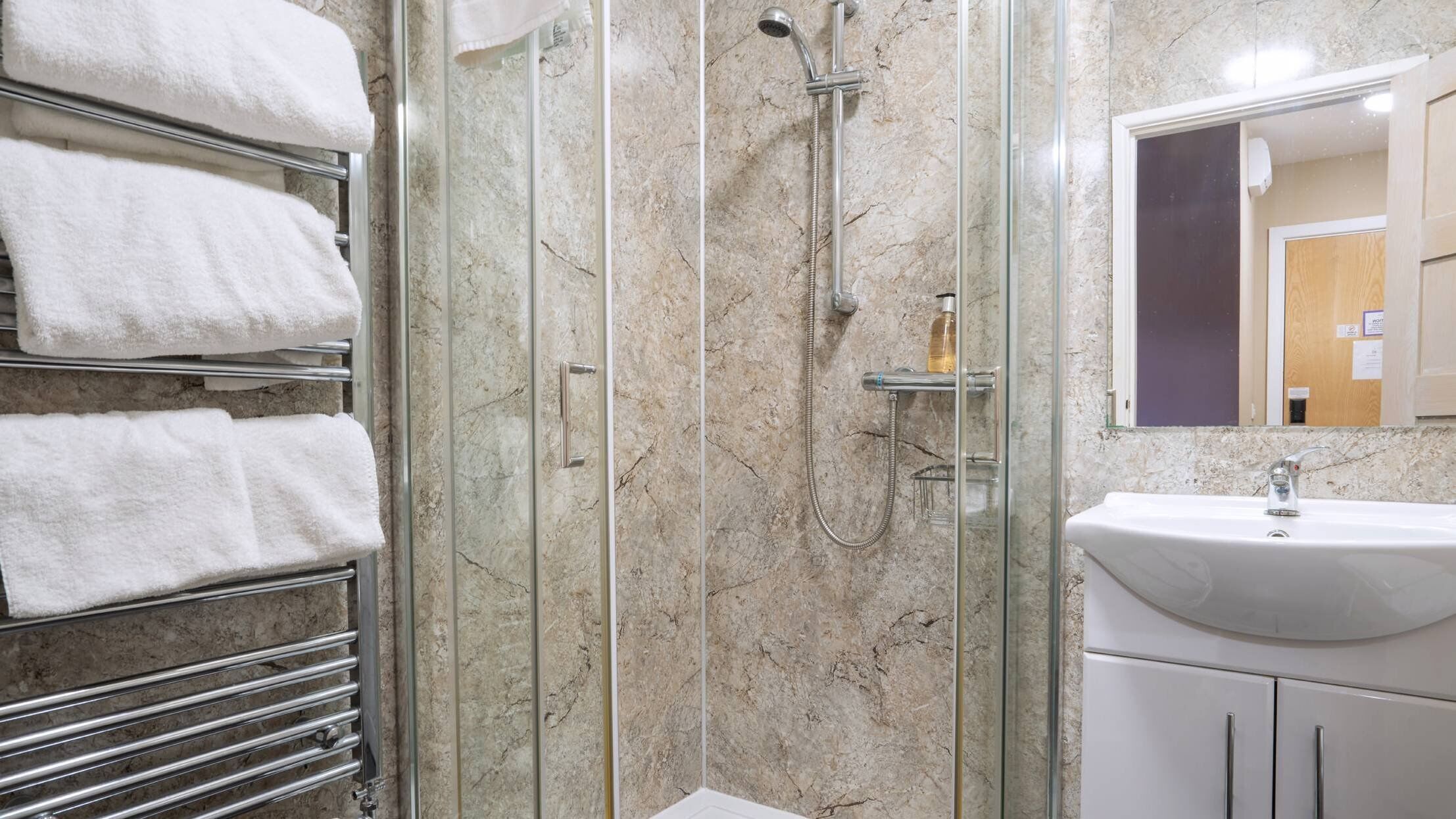 A modern bathroom with a glass-enclosed shower, a white sink, and a towel rack with neatly folded towels.