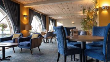 A hotel lobby with blue upholstered chairs, a wooden table, and a large potted plant.