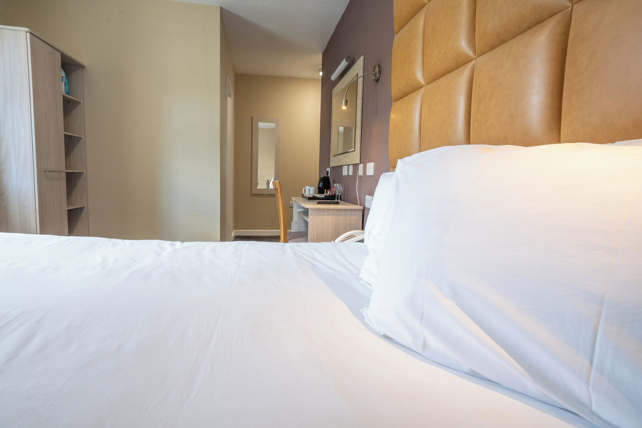 A hotel room with a large bed, a wooden wardrobe, a desk with a chair, and a mirror on the wall.