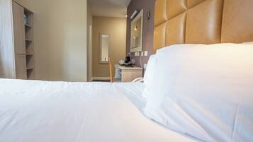 A hotel room with a large bed, a wooden wardrobe, a desk with a chair, and a mirror on the wall.