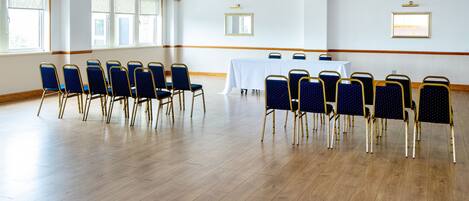 A conference room with rows of chairs, a table with a white tablecloth, and large windows with blinds.