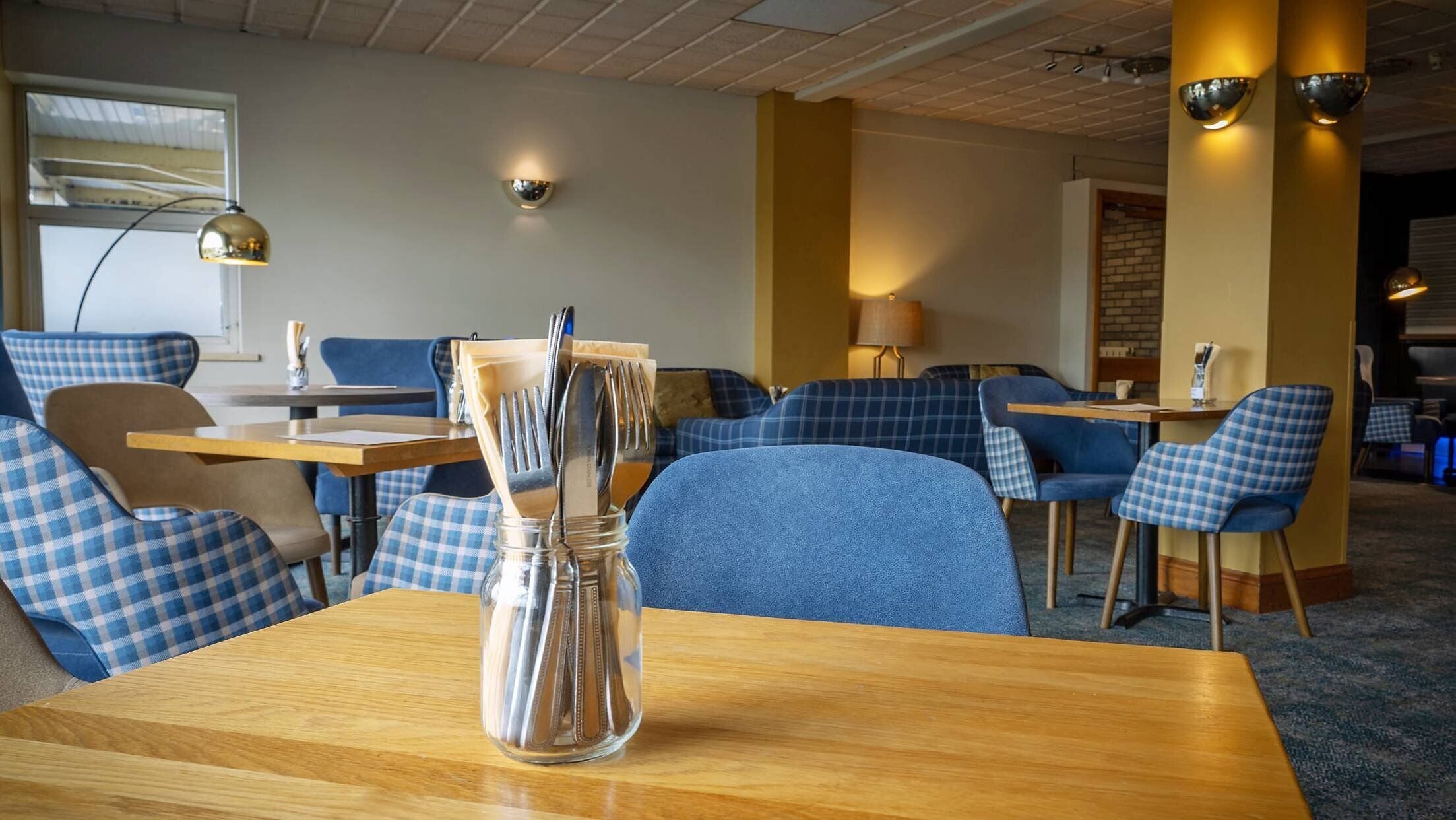 A dining area with checkered blue chairs, wooden tables, and a clear glass vase with utensils.