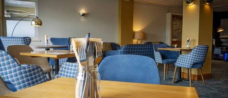 A dining area with checkered blue chairs, wooden tables, and a clear glass vase with utensils.