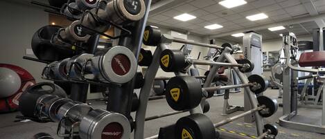 Un gimnasio con diverso equipamiento para levantamiento de pesas, incluyendo mancuernas y barras.