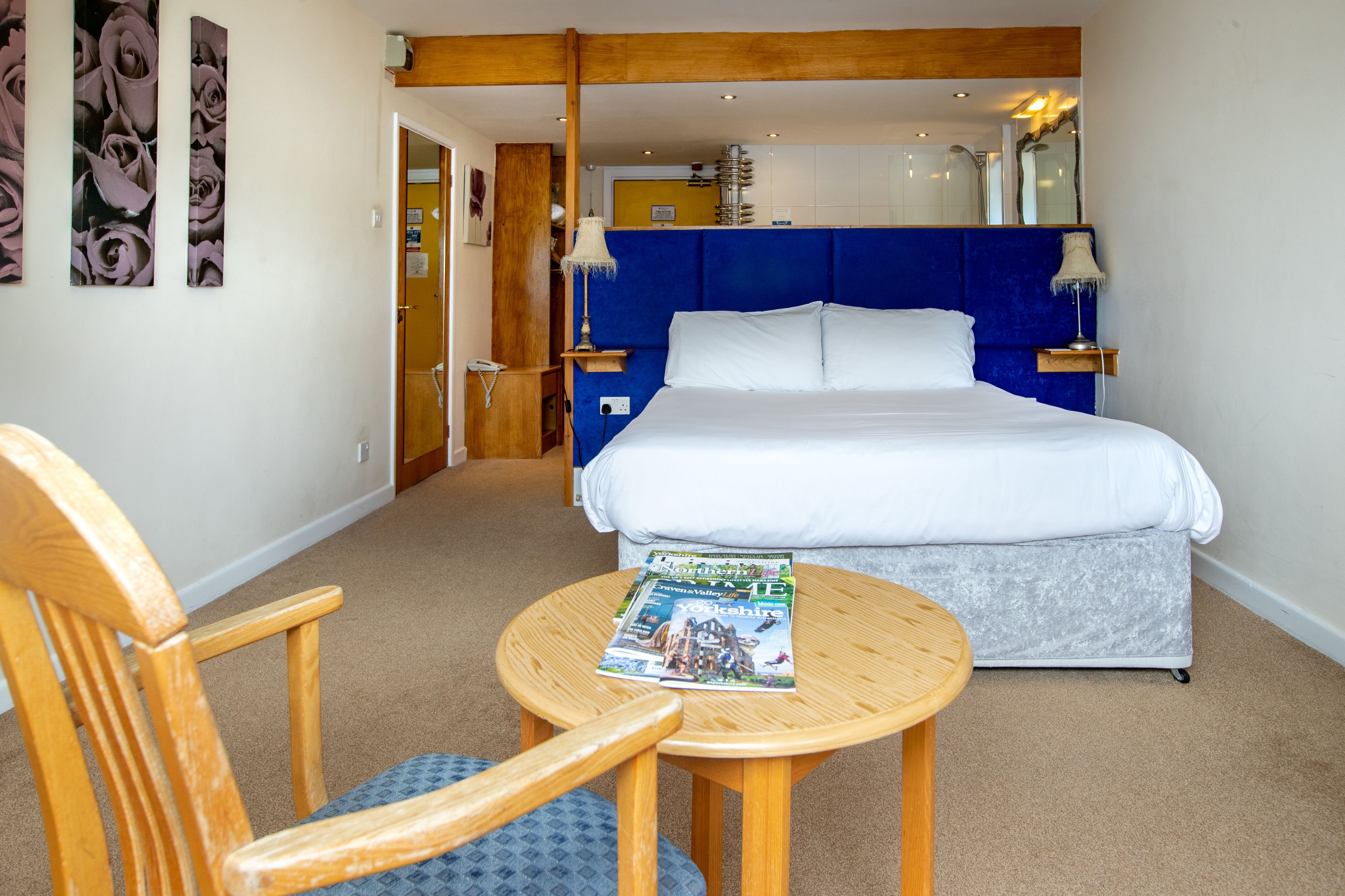 A bedroom with a bed, a wooden chair, a round table, and a magazine on the table.