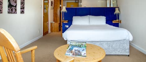 Une chambre à coucher avec un lit, une chaise en bois, une table ronde et un magazine posé sur la table.