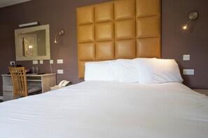 A hotel room with a large bed, a wooden headboard, a desk with a chair, a telephone, and a mirror.