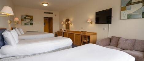 A hotel room with two single beds, a sofa, a desk with a chair, a flat-screen TV, and wall-mounted lamps.
