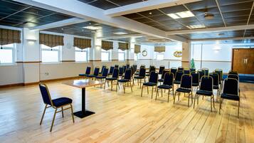 Une salle de conférence avec des rangées de chaises, un plancher en bois et de grandes fenêtres dotées de rideaux.