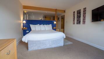 A bedroom with a large bed, bedside lamps, a wooden dresser, a flat-screen TV, and three wall-mounted paintings.