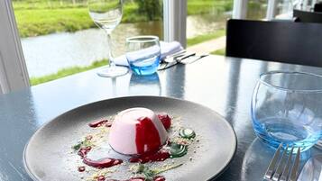A dessert on a plate with a glass of water and a fork on a table with a view of a river.