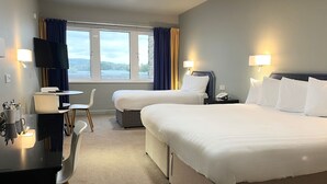 Habitación de hotel con dos camas, un escritorio con silla, televisión y ventana con cortinas.