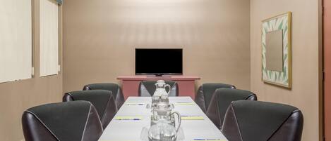 A conference room with a long table, six chairs, a TV, a pink desk, and a decorative mirror.
