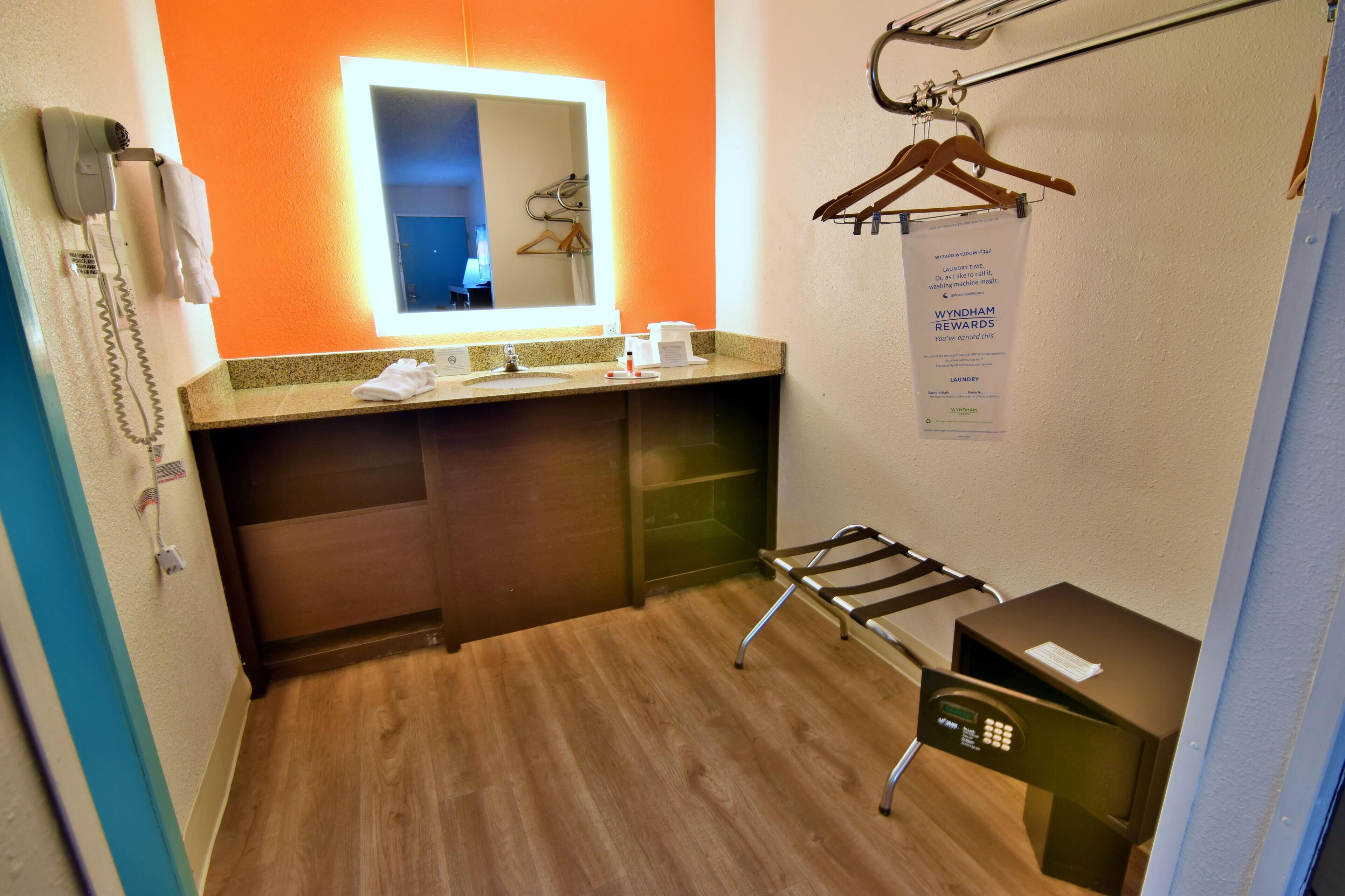 Ein kleines Badezimmer in einem Hotel mit Holzboden, Waschbecken mit Ablagefläche, Spiegel, Fön und Handtuchhalter.