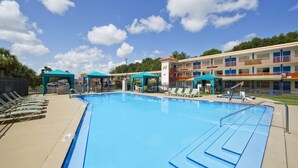 Ein Schwimmbecken mit Liegestühlen und ein Gebäude im Hintergrund mit mehreren Balkonen.