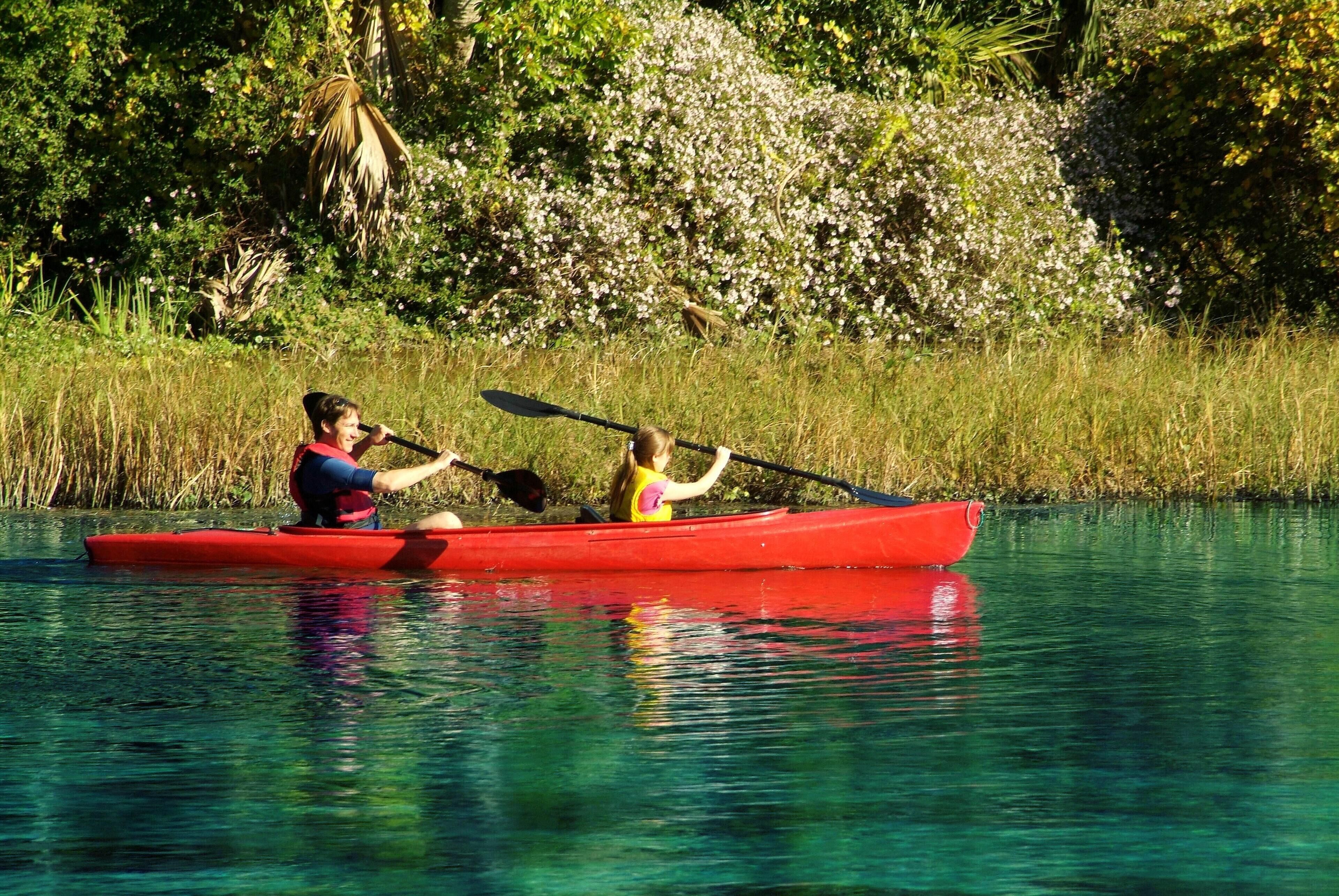 Two people kayaking in a red canoe on a calm body of water surrounded by lush greenery.