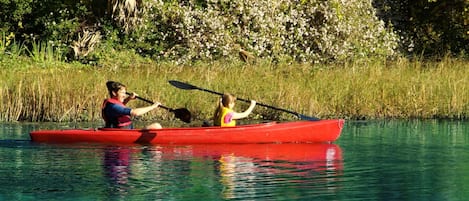 Two people kayaking in a red canoe on a calm body of water surrounded by lush greenery.