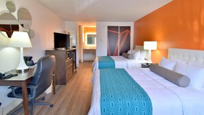 Ein Hotelzimmer mit zwei Betten, einem Schreibtisch mit Stuhl, einem Fernseher und einem im Hintergrund sichtbaren Badezimmer.