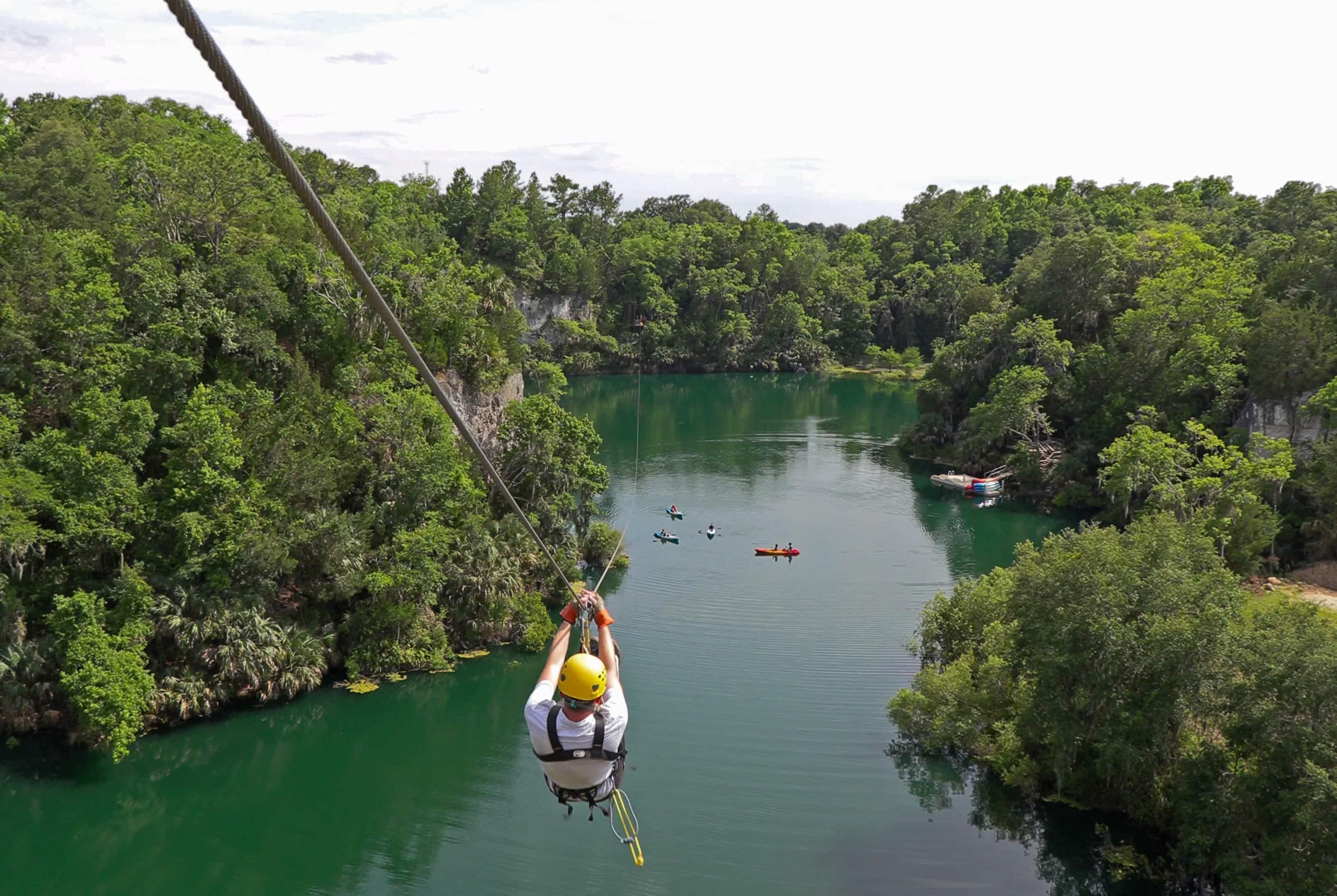 A person zip-lining over a river surrounded by dense forest.