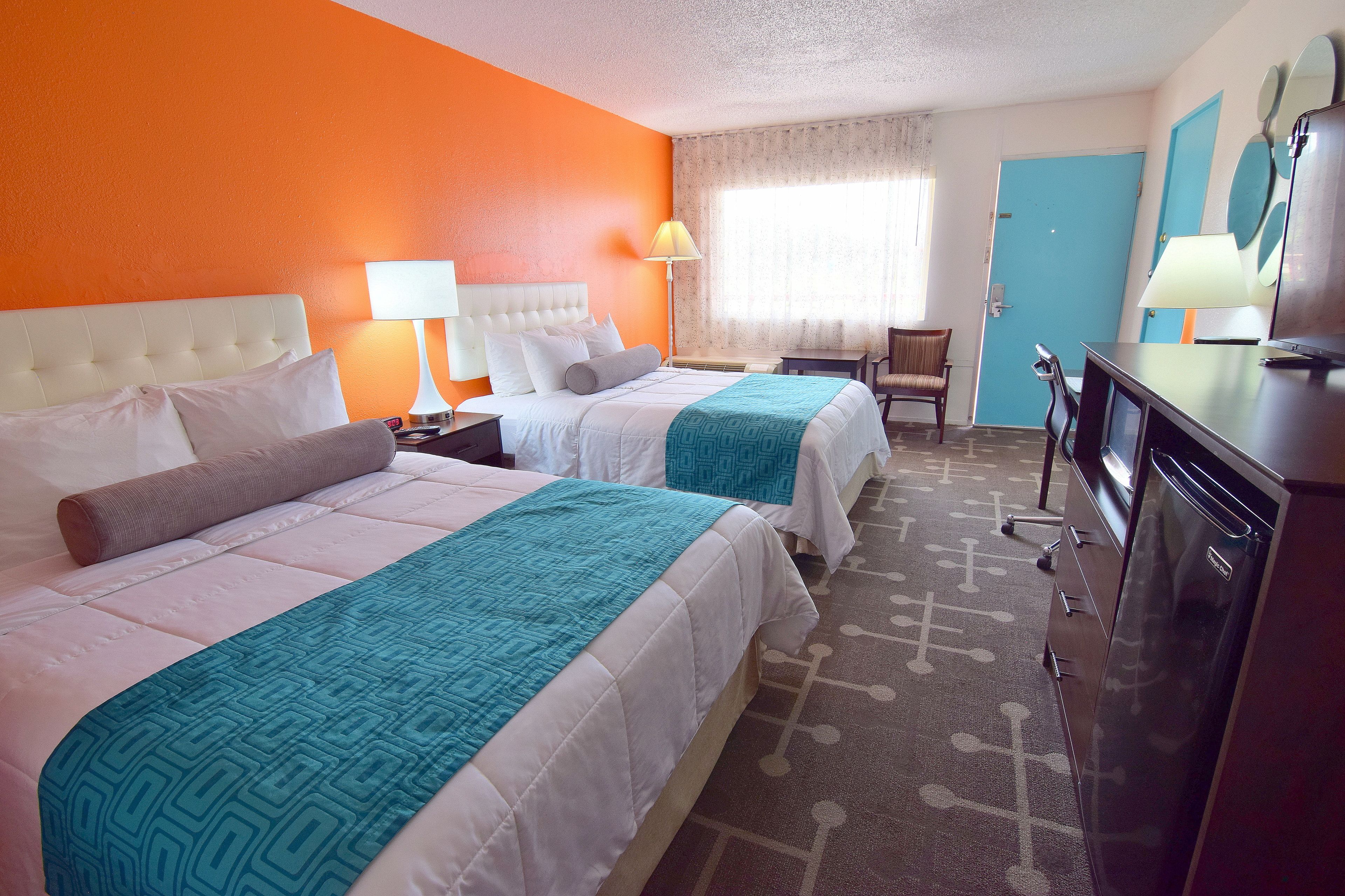 A hotel room with two beds, a desk, a chair, and a TV.