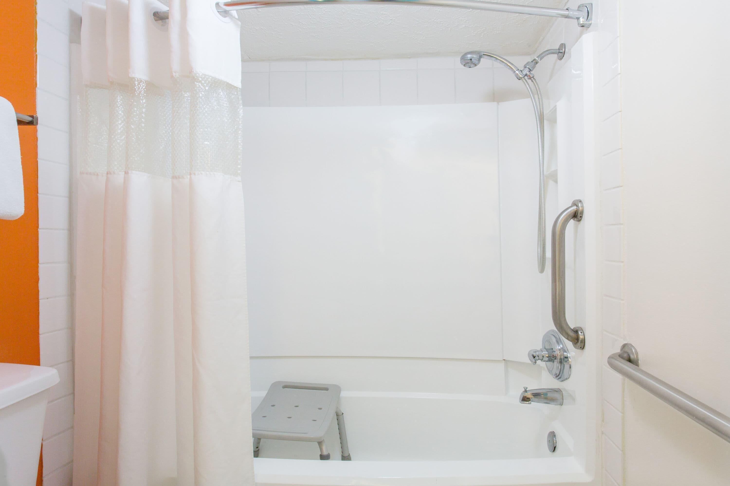 A shower area with a handheld showerhead, a handheld shower control, and a step stool.