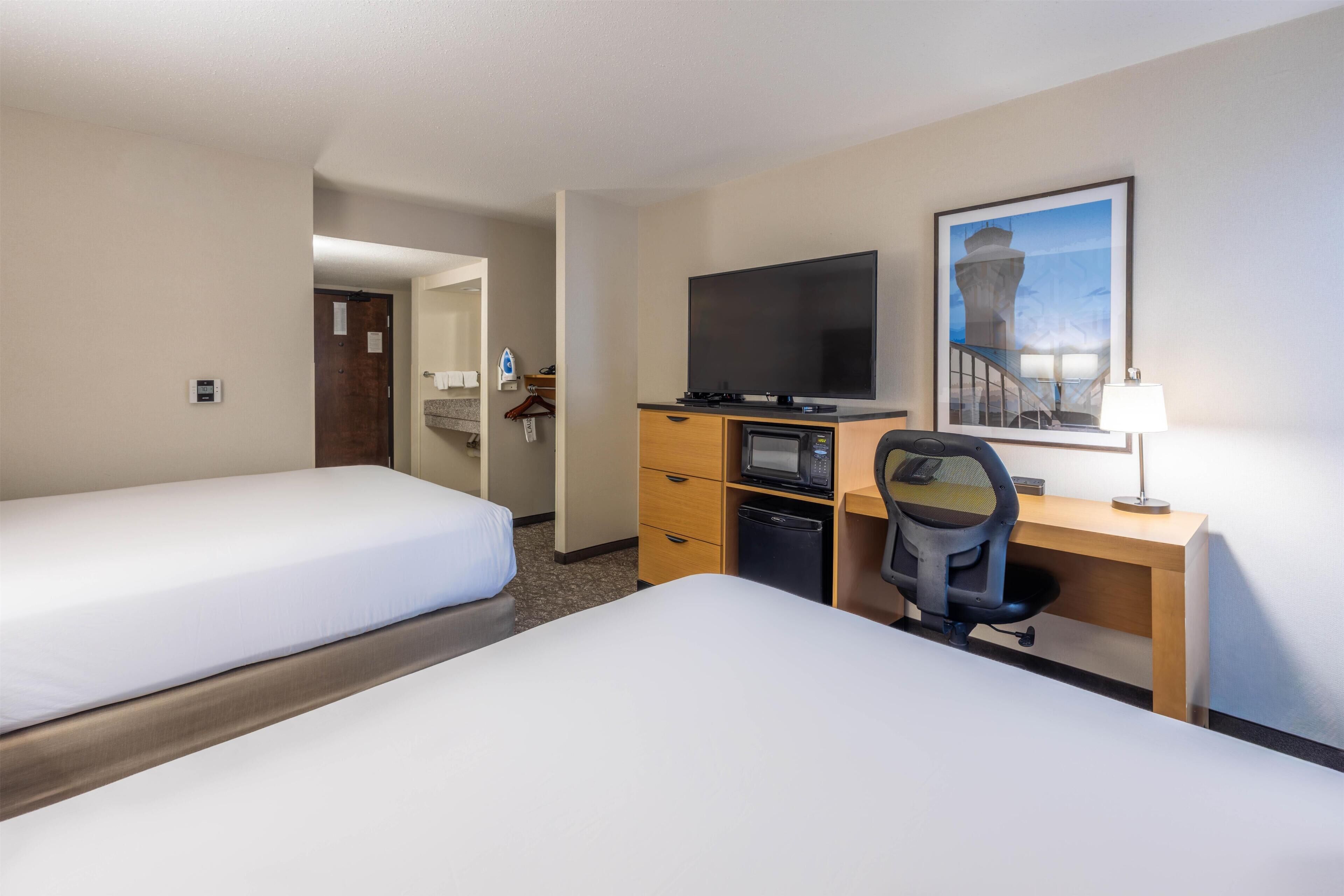 A hotel room with two beds, a desk with a computer, a television, and a framed picture on the wall.