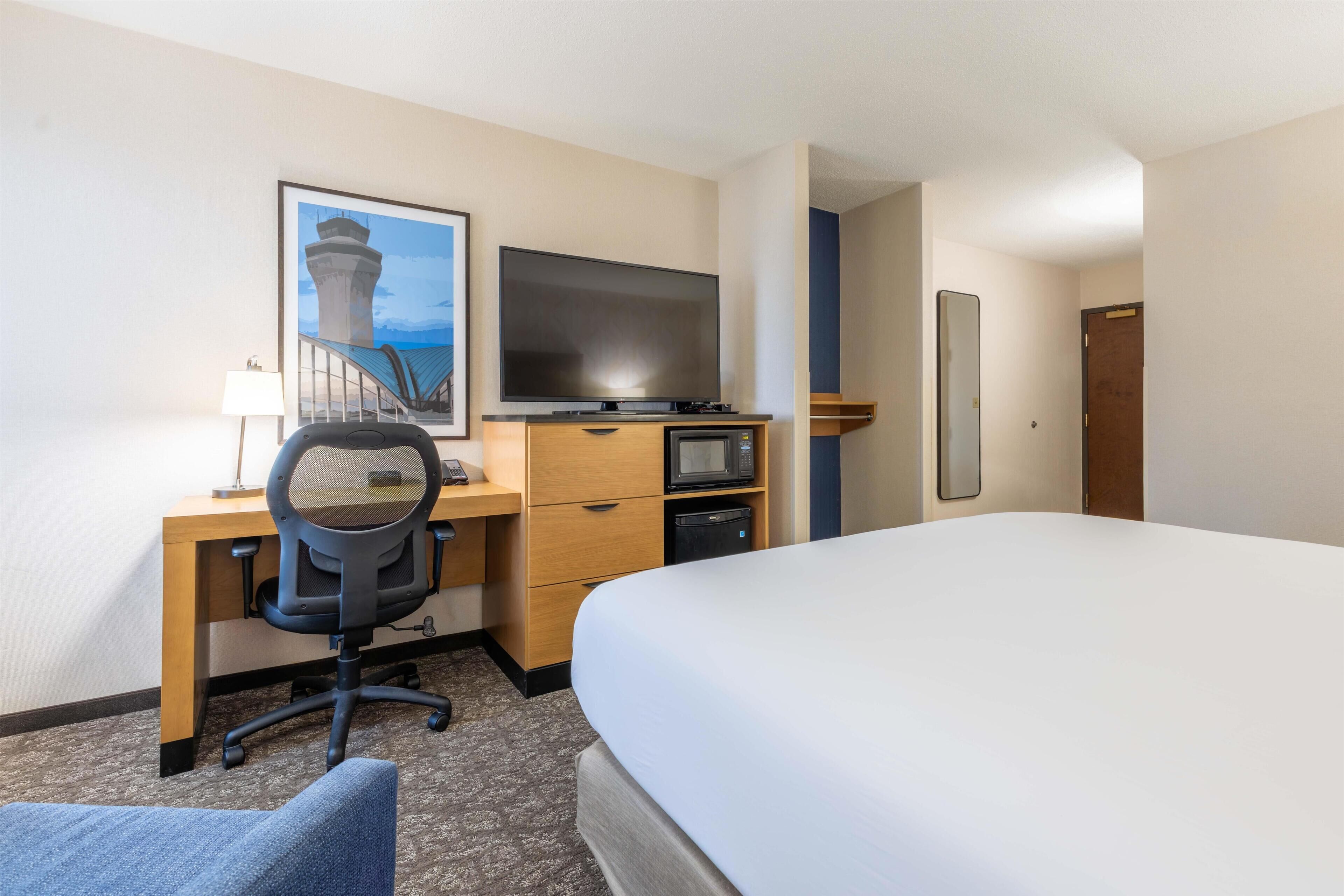 Een hotelkamer met een bed, bureau, stoel, televisie, magnetron en een lijst aan de muur.