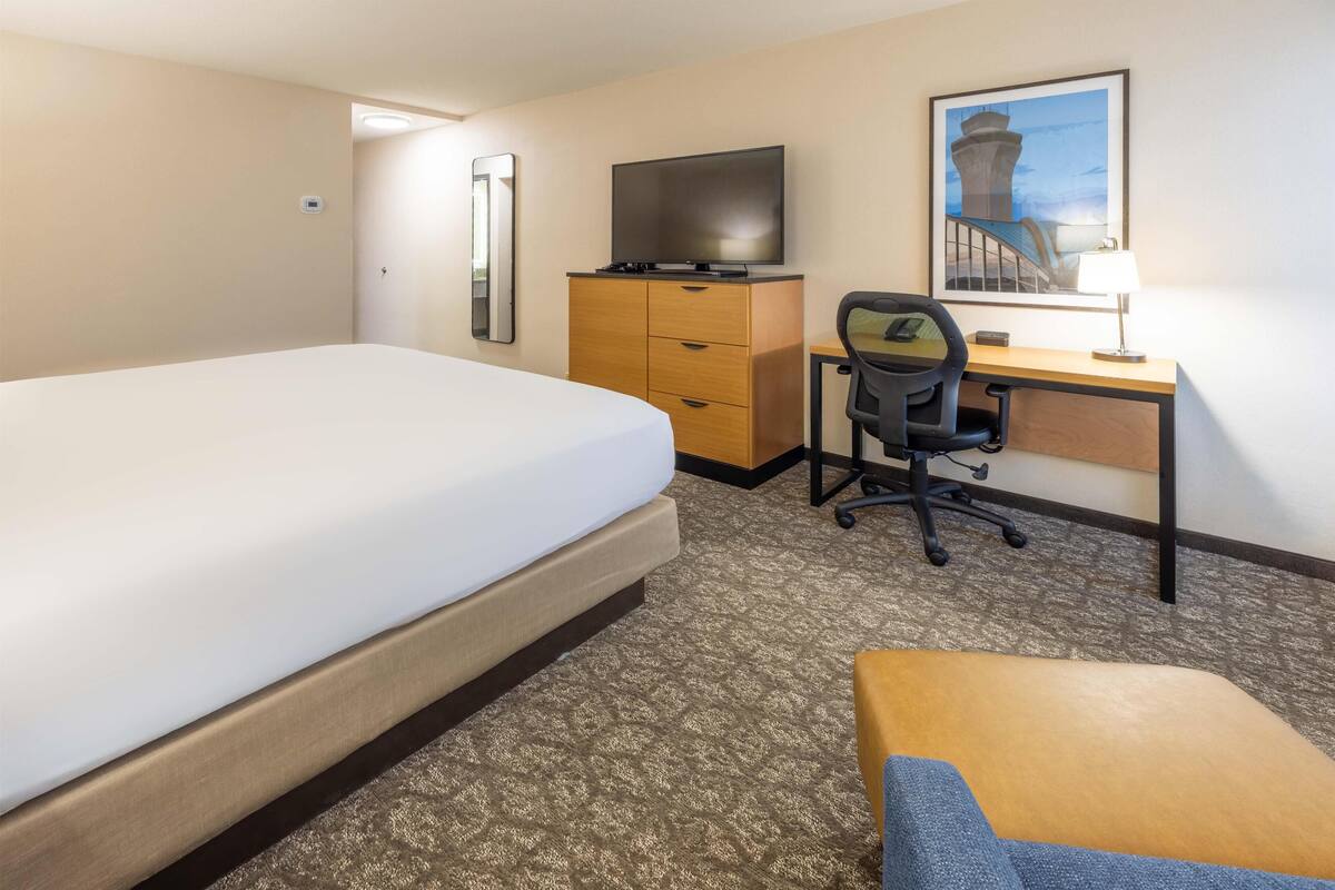 A hotel room with a bed, a desk with a chair, a television, a desk lamp, and a framed picture on the wall.