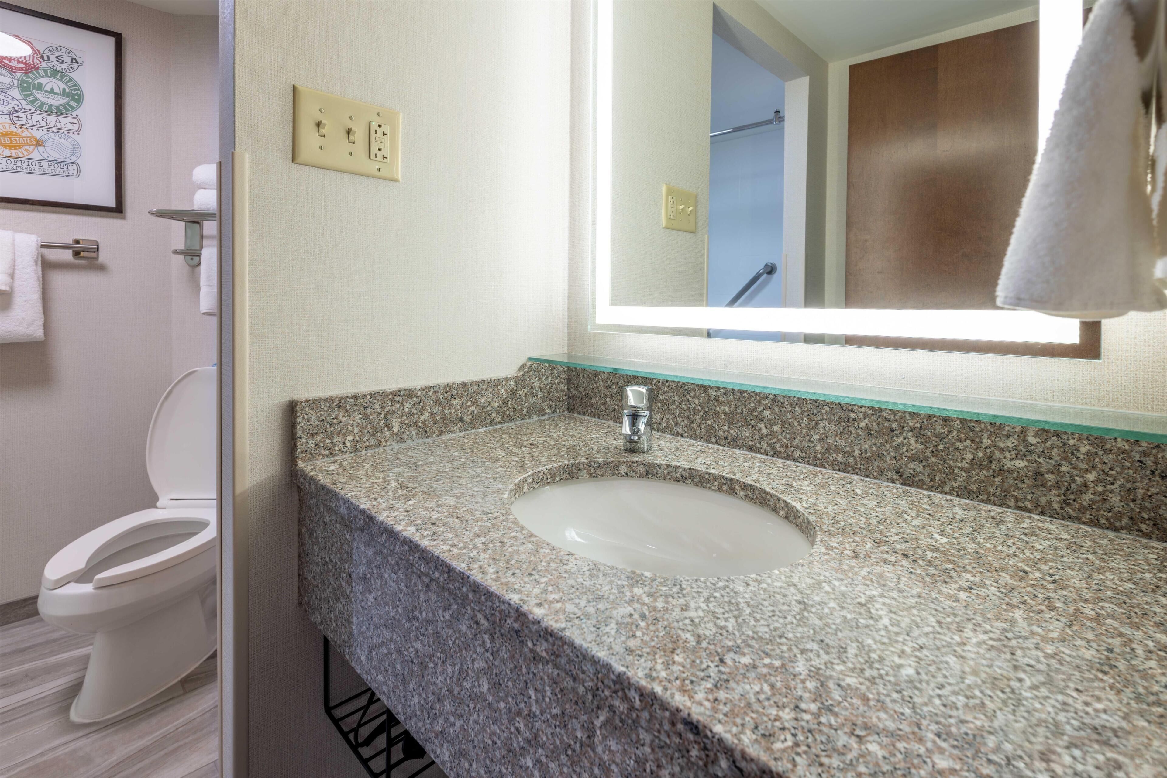 A bathroom with a granite countertop, a sink, a mirror, and a toilet.