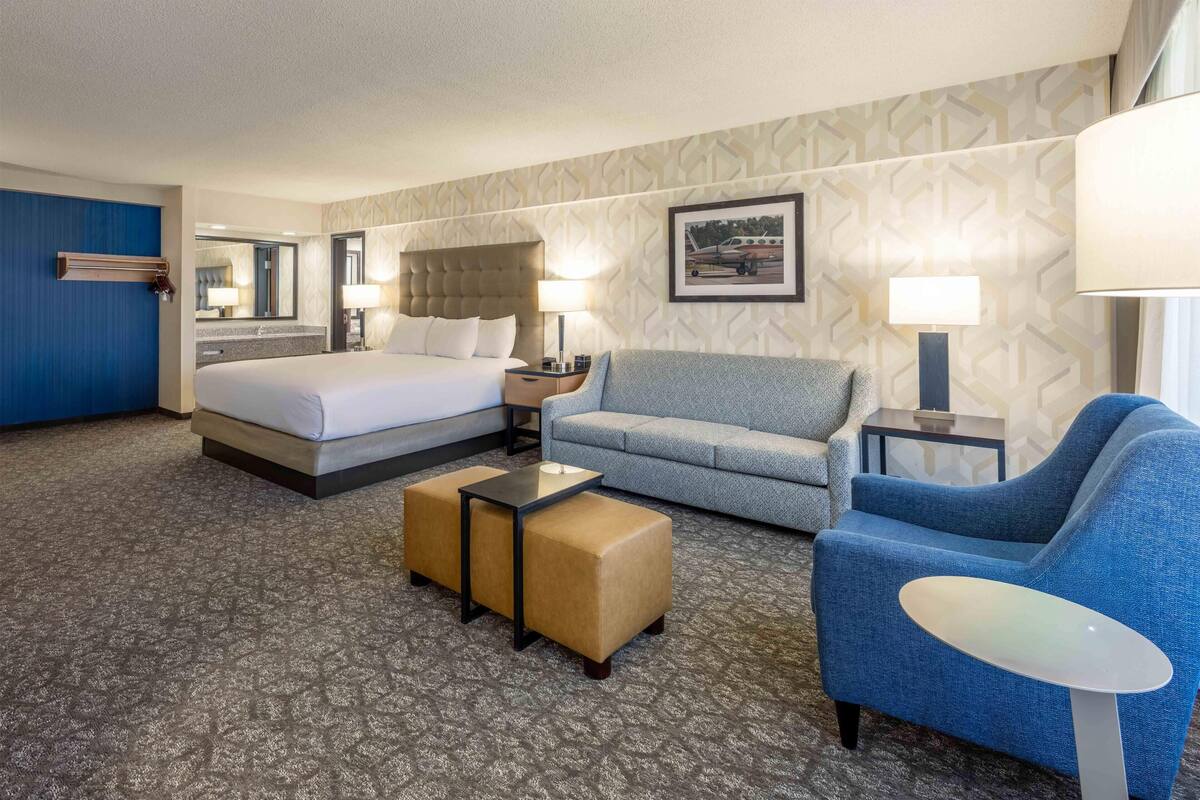 A hotel room with a bed, two armchairs, a sofa, a small table, and a nightstand.
