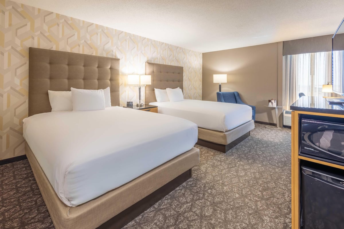 A hotel room with two beds, a desk, a chair, and a minibar.