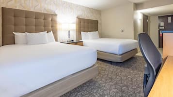 Quarto de hotel com duas camas, uma escrivaninha e uma cadeira.