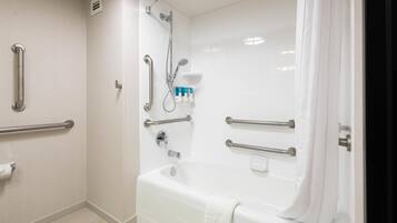 A bathroom with a bathtub, handrails, a shower, and a toilet.