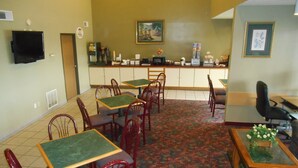 A restaurant with green tables and red chairs, a counter with a coffee machine, and a painting on the wall.