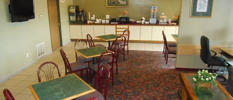 Un restaurante con mesas verdes y sillas rojas, una barra con máquina de café y un cuadro en la pared.