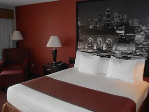 Een hotelkamer met een groot bed, een rode wand en een stadsgezicht schilderij erboven.
