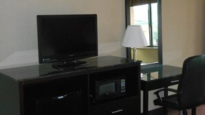 A hotel room with a television, a lamp, a microwave, and a desk with a chair.