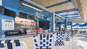 A beachside bar with a blue and white color scheme, a W-KING audio system, and a CINTAS First Aid Center sign. - Hilton Vacation Club Charter Club Naples Bay (Naples)
