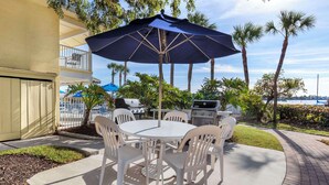 An outdoor patio with a round table and chairs, a grill, and a large umbrella. - Hilton Vacation Club Charter Club Naples Bay (Naples)