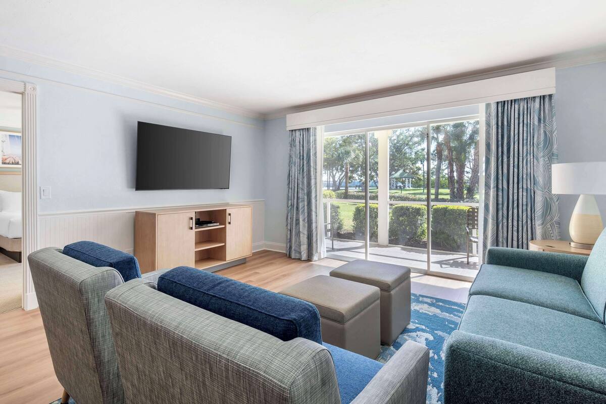A modern living room with a flat-screen TV, a wooden cabinet, and a large sliding glass door leading to a balcony.