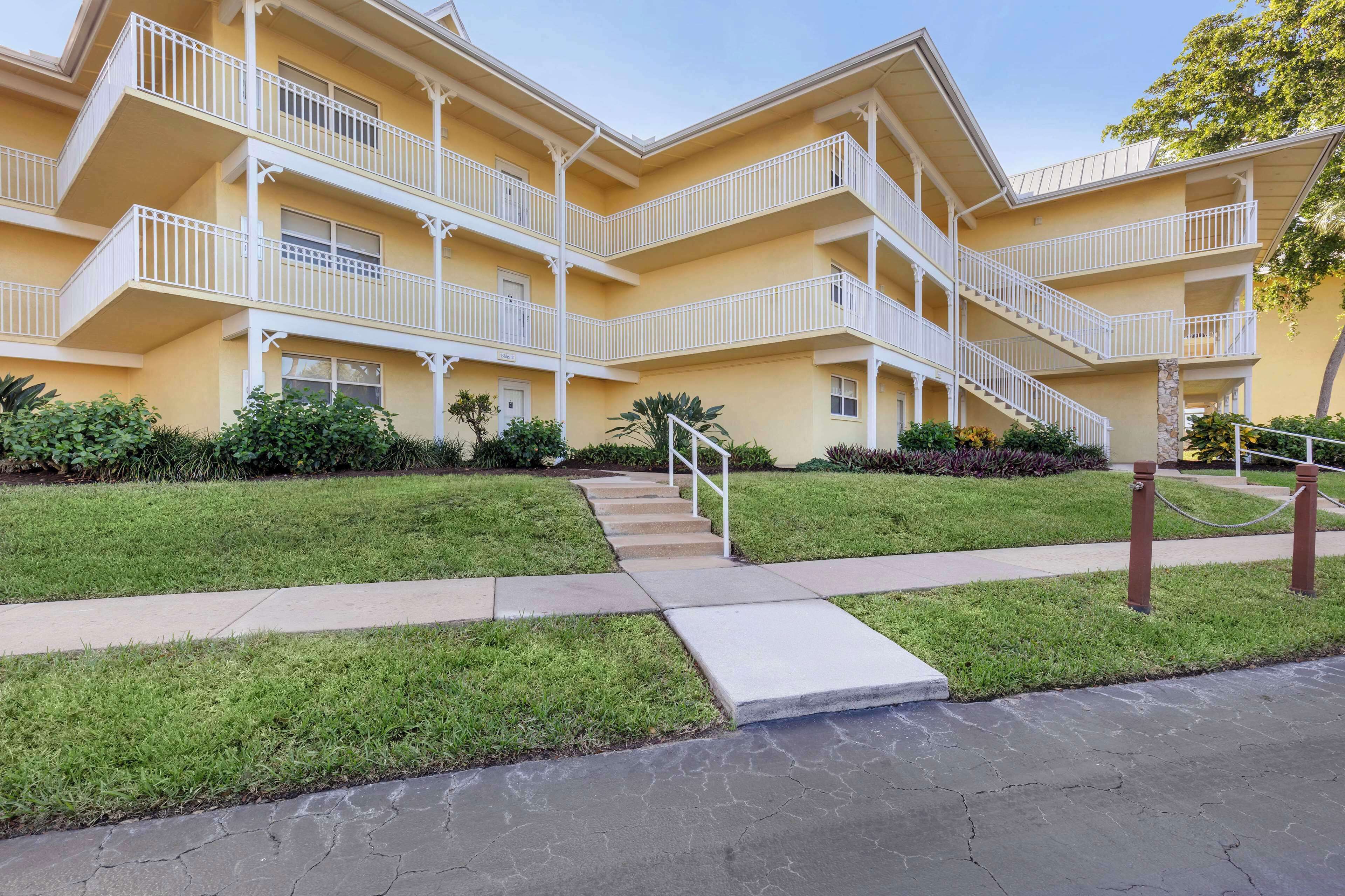 A multi-story hotel with balconies, a central staircase, and a well-maintained lawn.