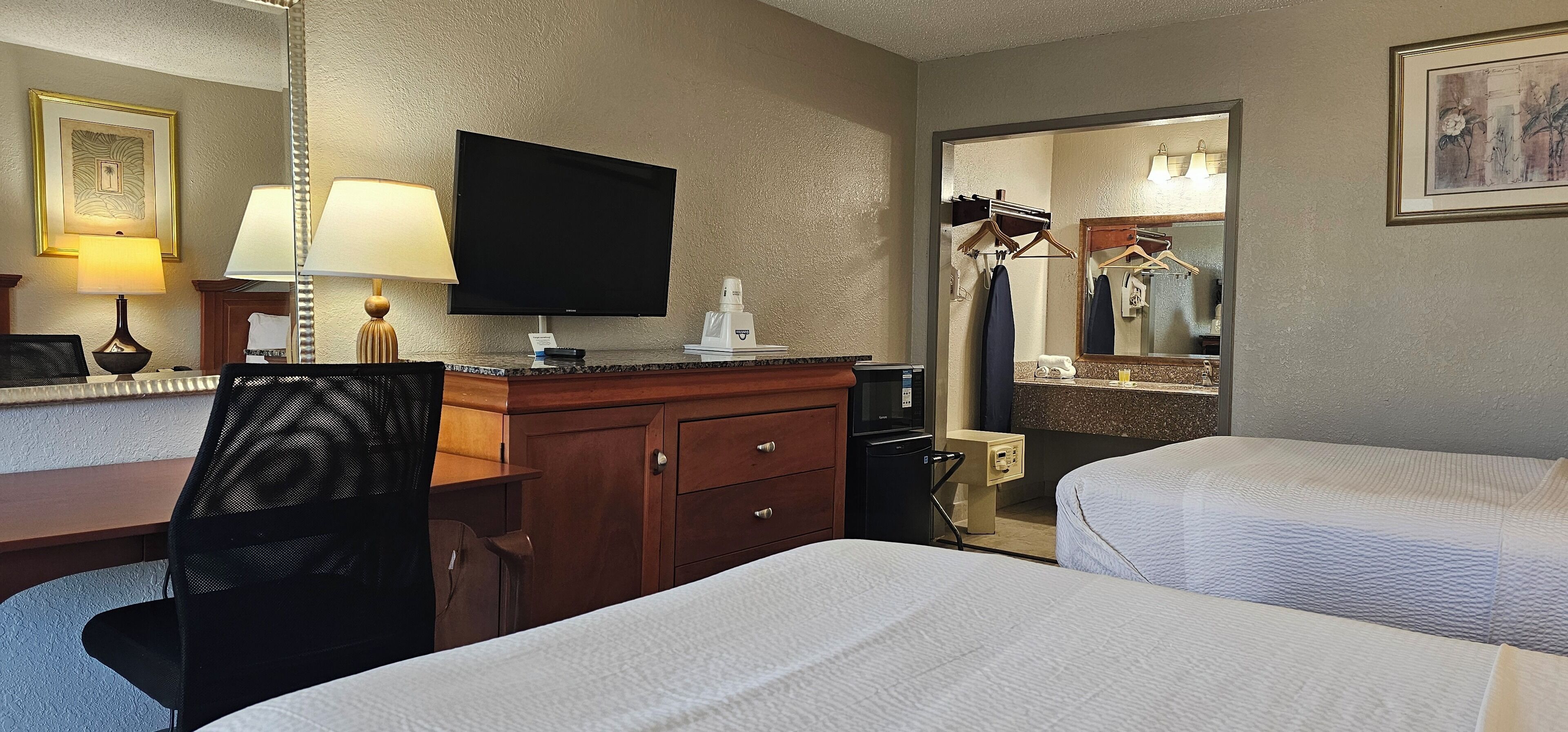 Een hotelkamer met twee bedden, een bureau met stoel, een televisie, een spiegel en een kleine tafeltje met lamp.