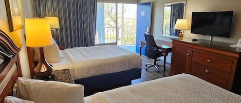 A hotel room with two beds, a desk, a chair, a television, and a balcony with curtains.