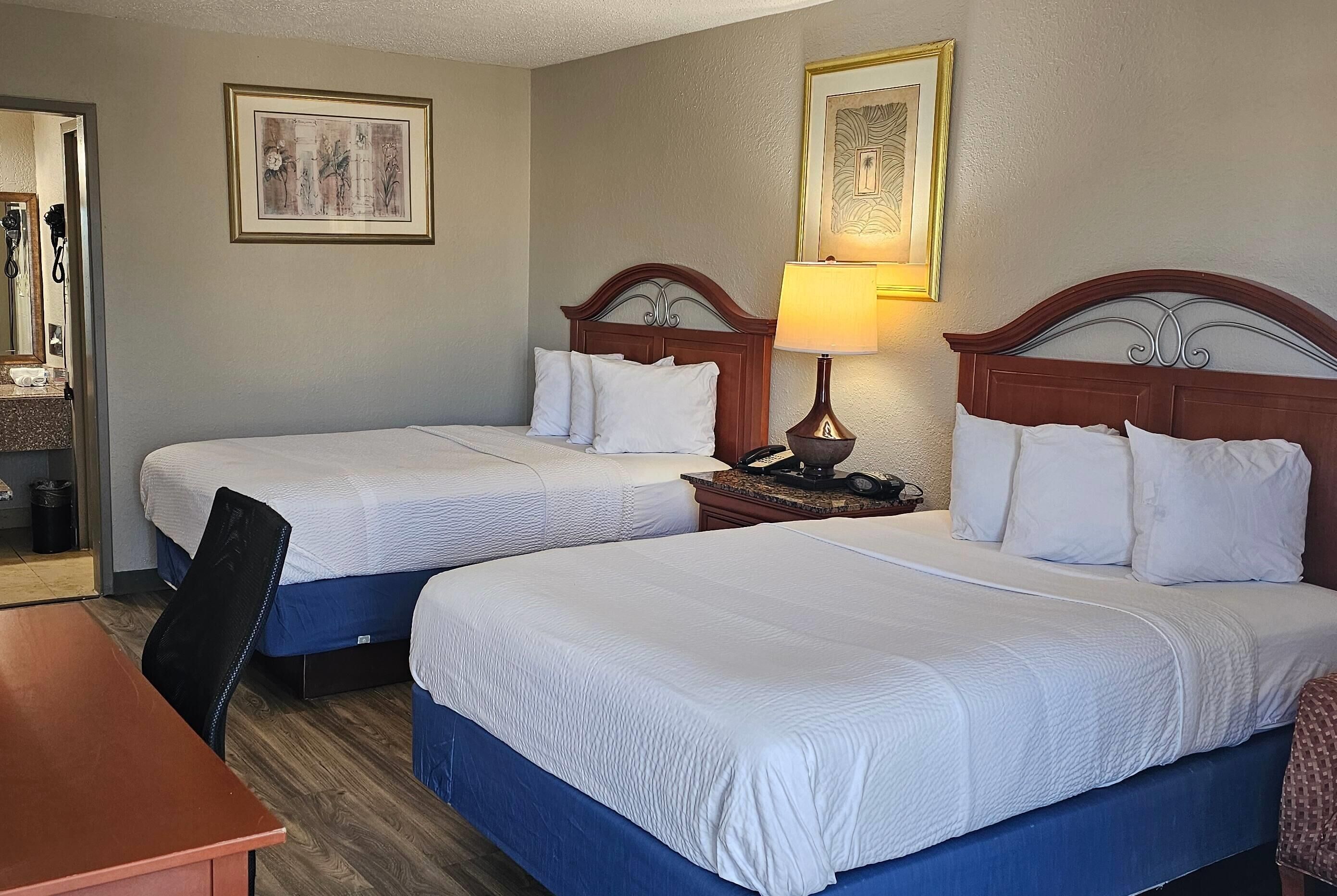 A hotel room with two beds, a desk, and a mirror.