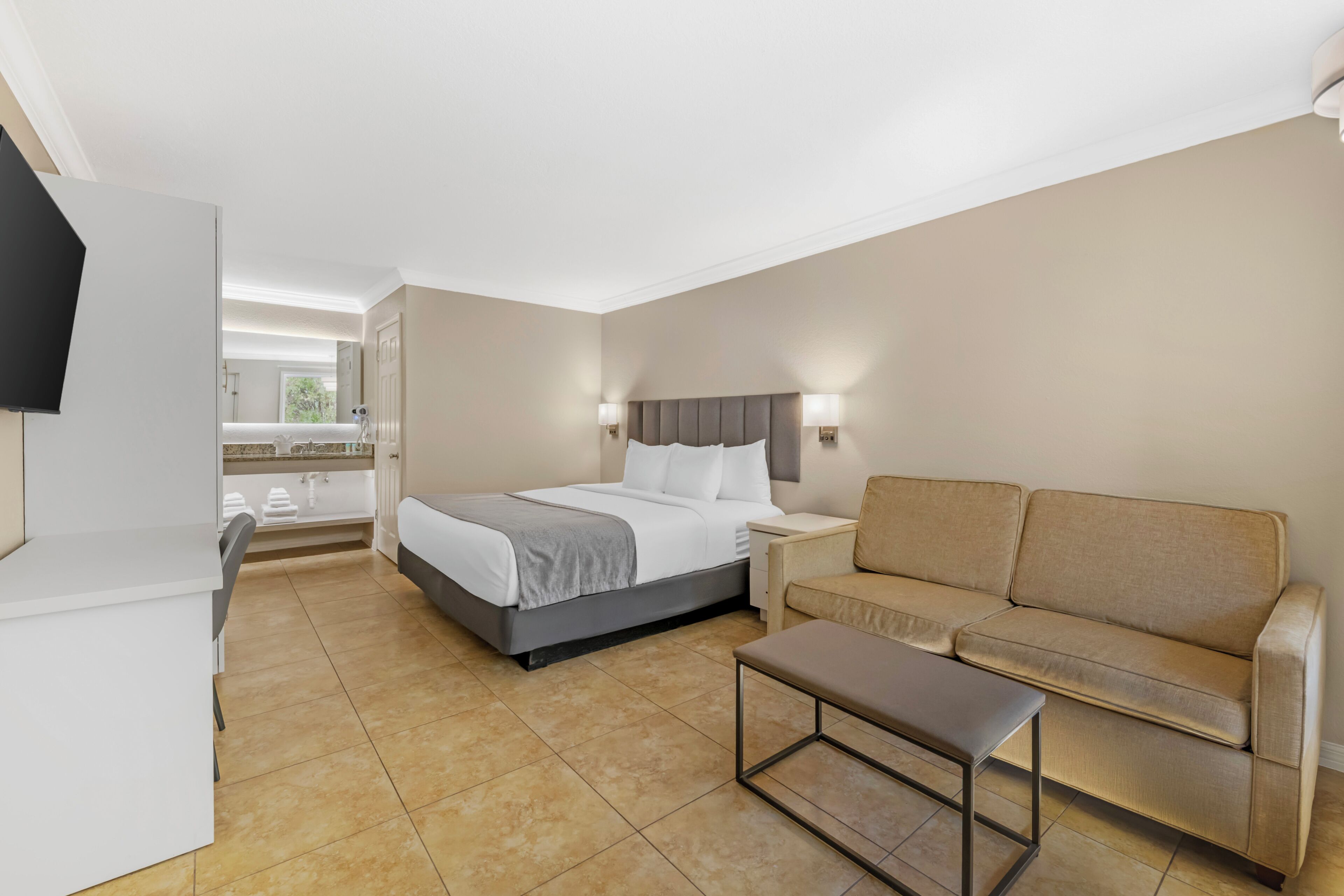 A hotel room with a bed, a sofa, a small table, and a TV.
